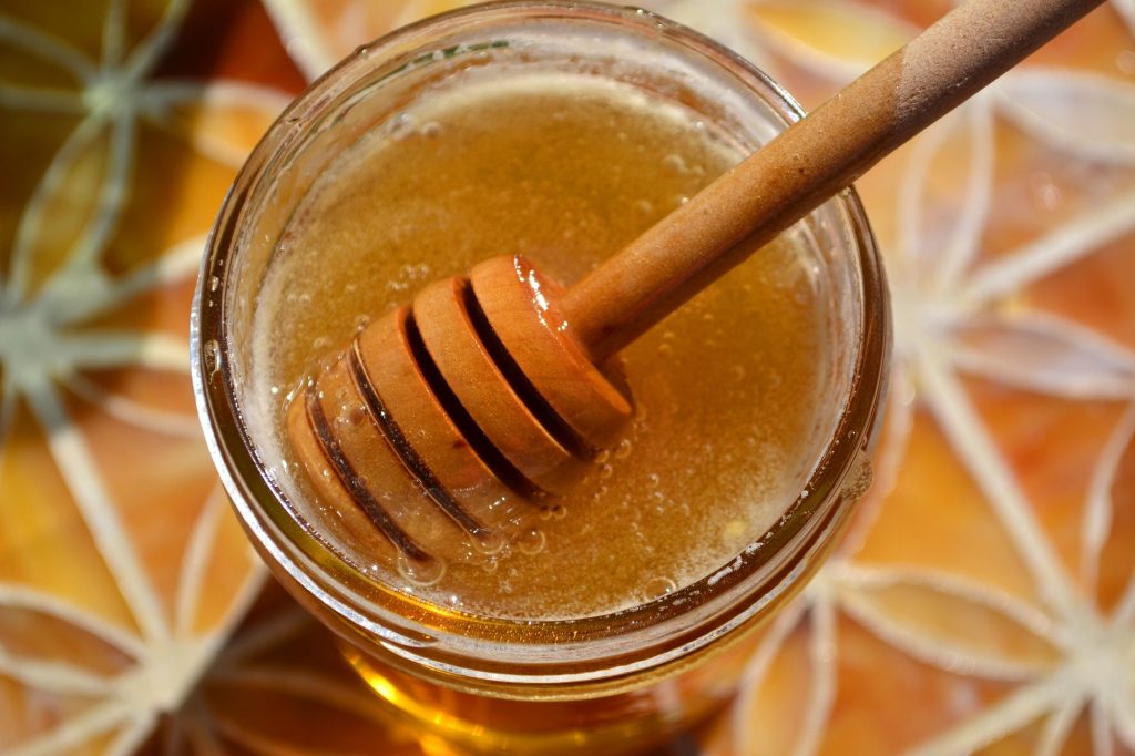 Fresh raw honey with a honey dipper in it. Amber, brown, golden