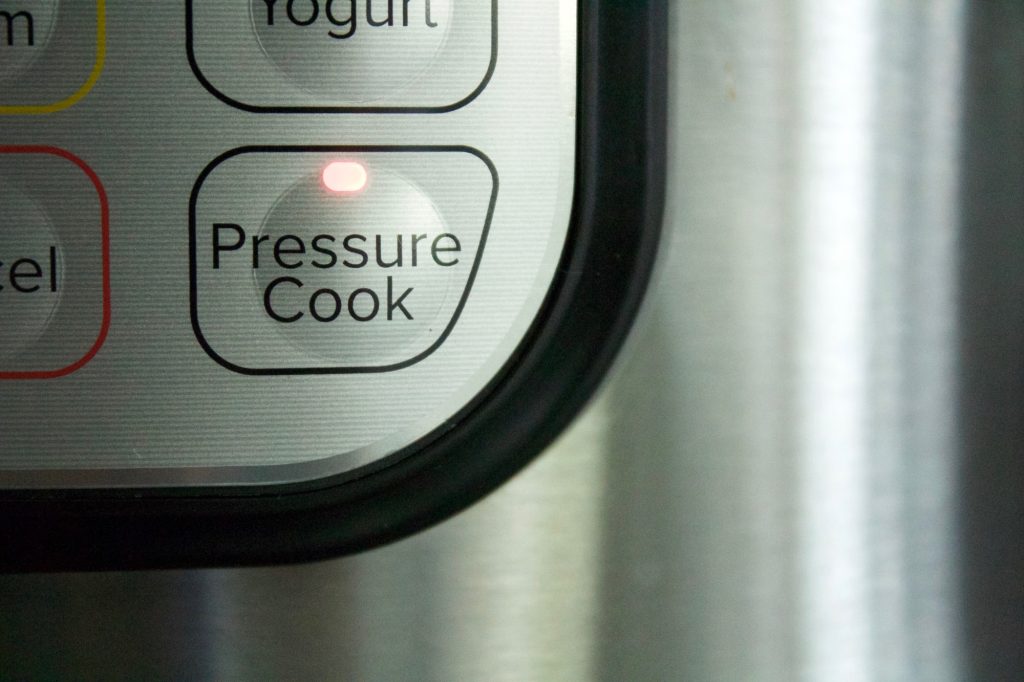 Closeup of illuminated pressure cook function button on stainless steel electric pressure cooker pot