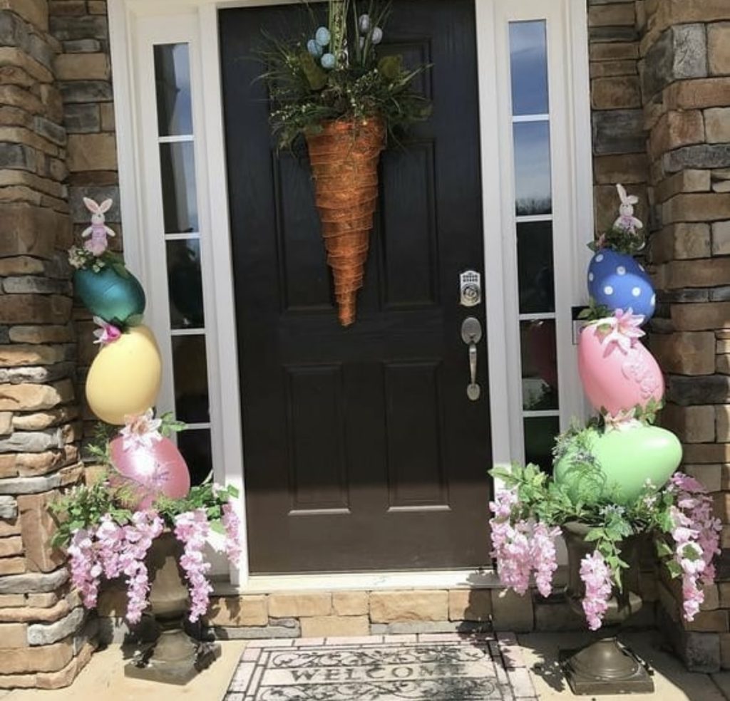 A carrot themed wreath with easter eggs and flowers in vases