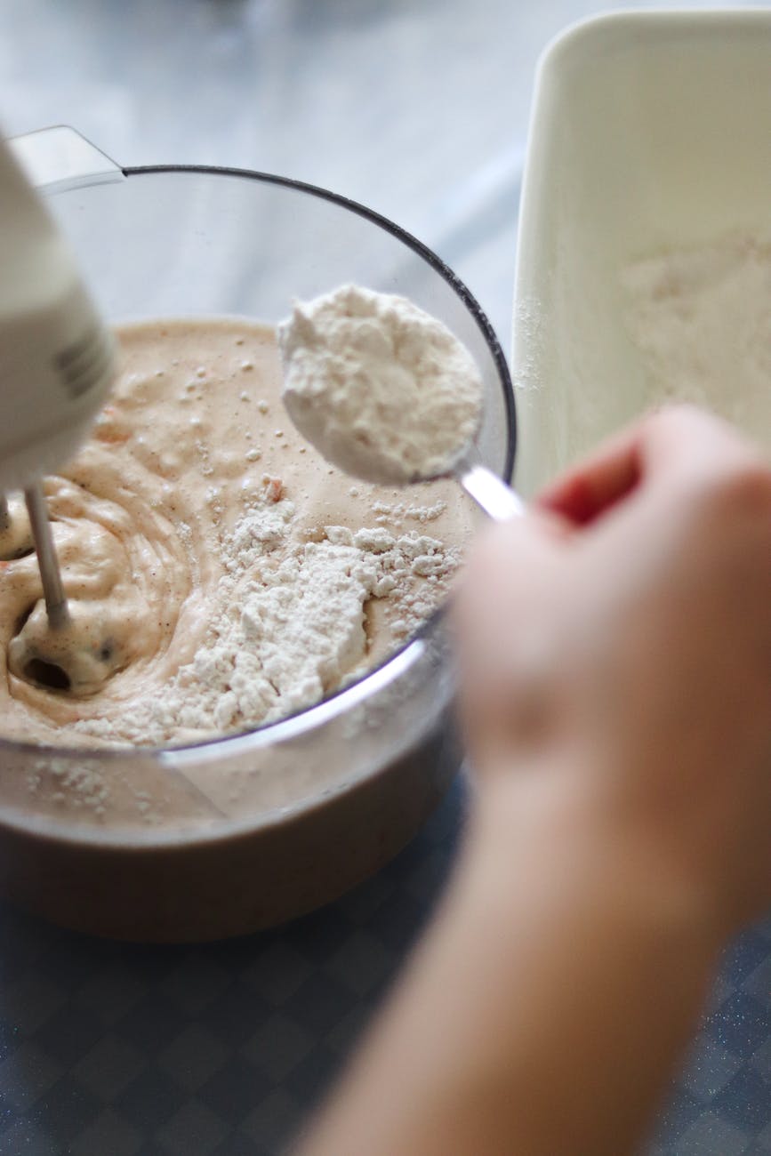 crop baker adding flour to dough while using mixer